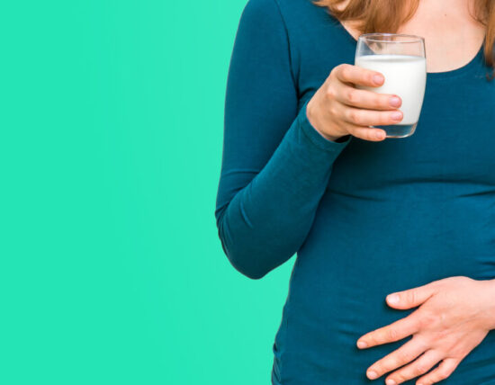 Vrouw met een glas melk en haar hand op haar onderbuik